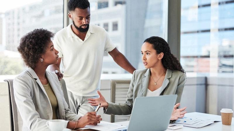 Three people at work in front of a laptop.