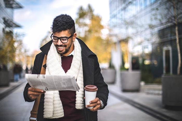 Person reading newspaper while holding coffee