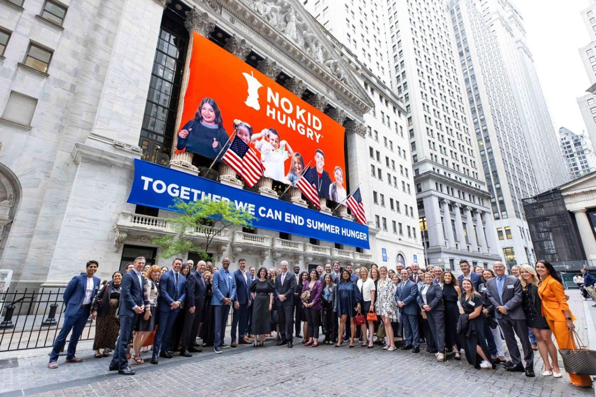 Group of supporters for No Kid Hungry standing outside No Kid Hungry banner on the front of the New York Stock Exchange
