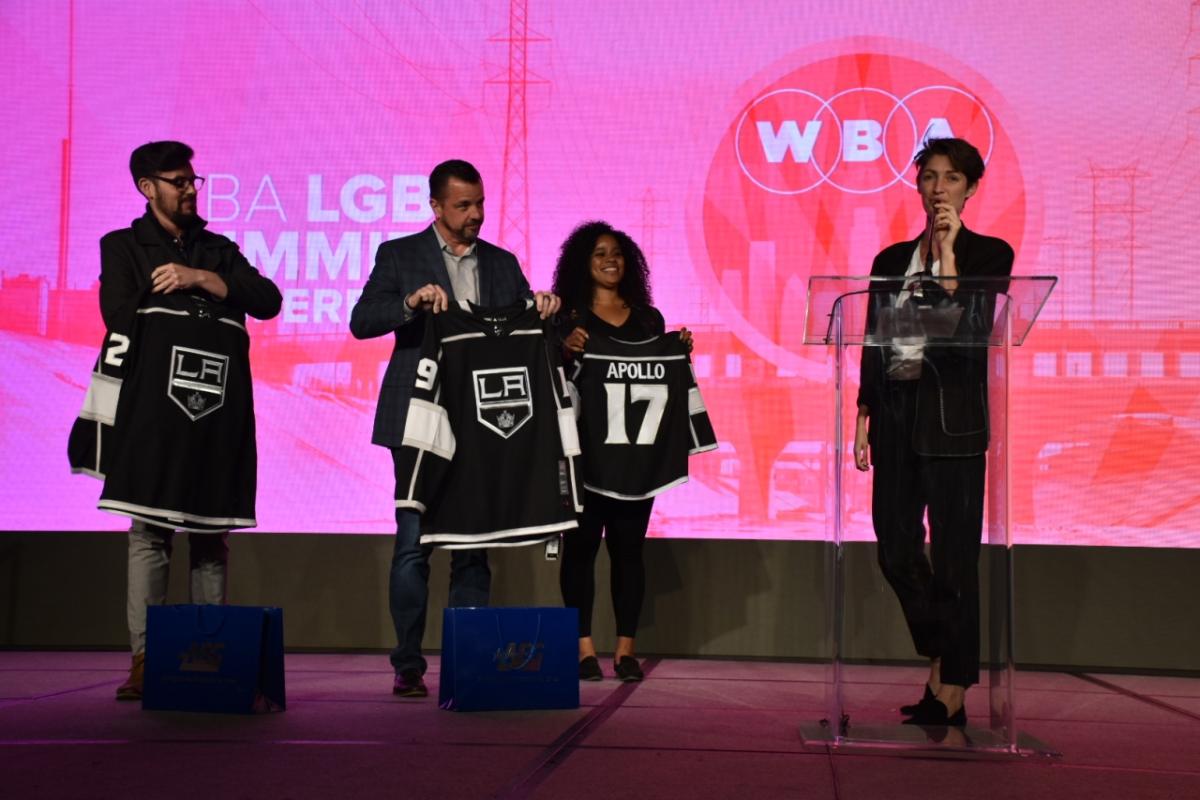 Emma Toshack (right), one of the founders of Nomadica, the business selected to participate in AEG's Inaugural Capacity Building Program, is presented with personalized LA Kings jerseys from members of AEG at the WBA LGBT Economic Impact Summit on March 15, 2019.