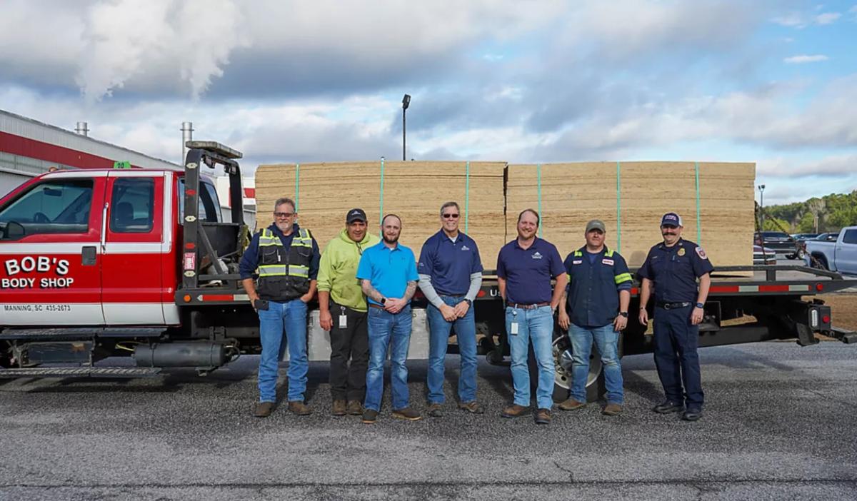 A group of seven people in front of a truck with loads of OSB boards on the trailer.