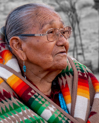 an elderly person sitting outside, a blanket wrapped around their shoulders