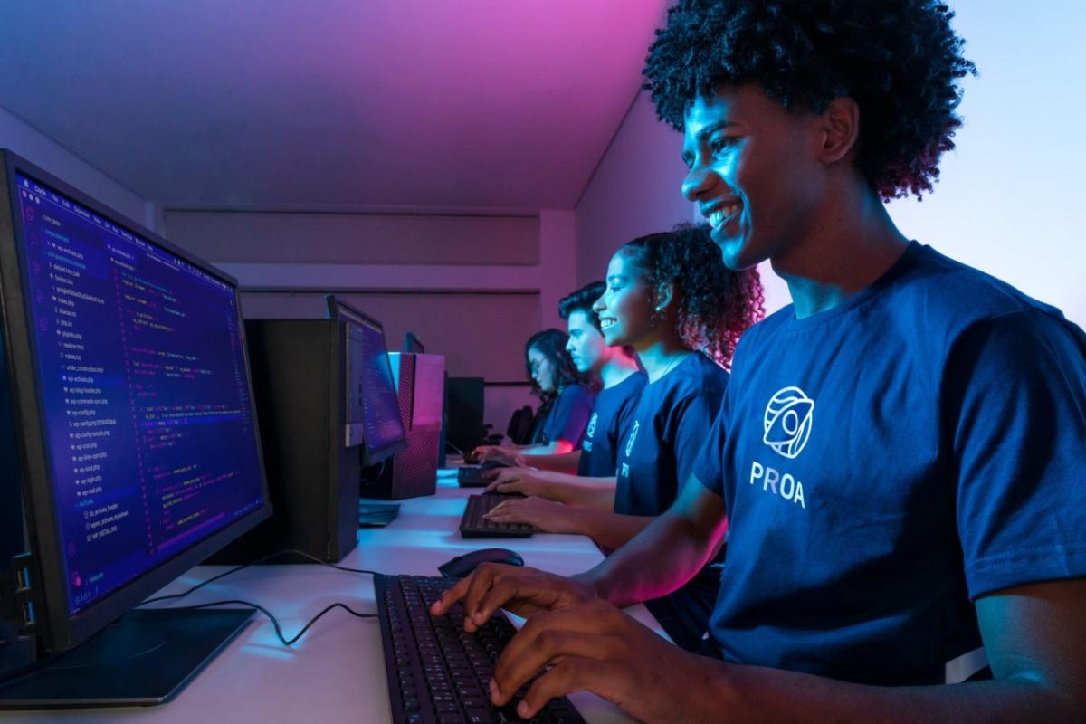 Students at a long table in a dark room, each using a desktop computer.