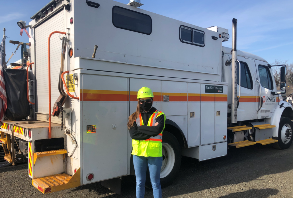 PSEG female employee standing in front of a PSEG service vehicle wearing safety gear, mask and hardhat.