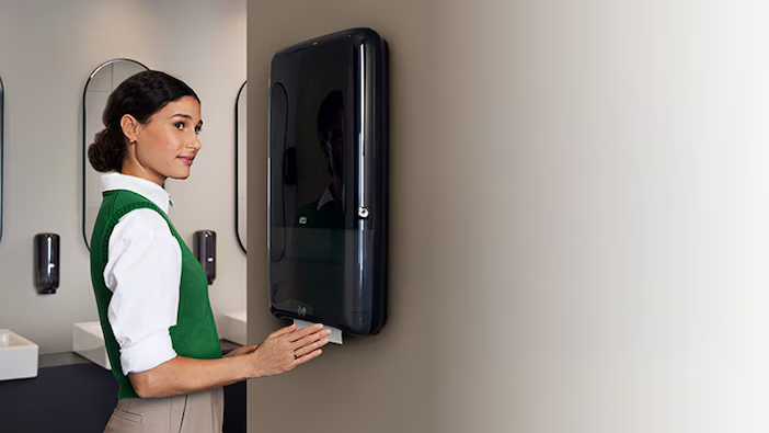 A person shown at a paper towel dispenser.