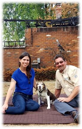 Claire Stevens sits in front of her fire-damaged home with her dog Pearl and Consumers Energy’s Guy Houseman, who helped ensure Pearl was rescued.