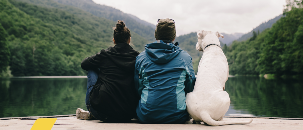 Two people sat with their dog looking out on to a lake