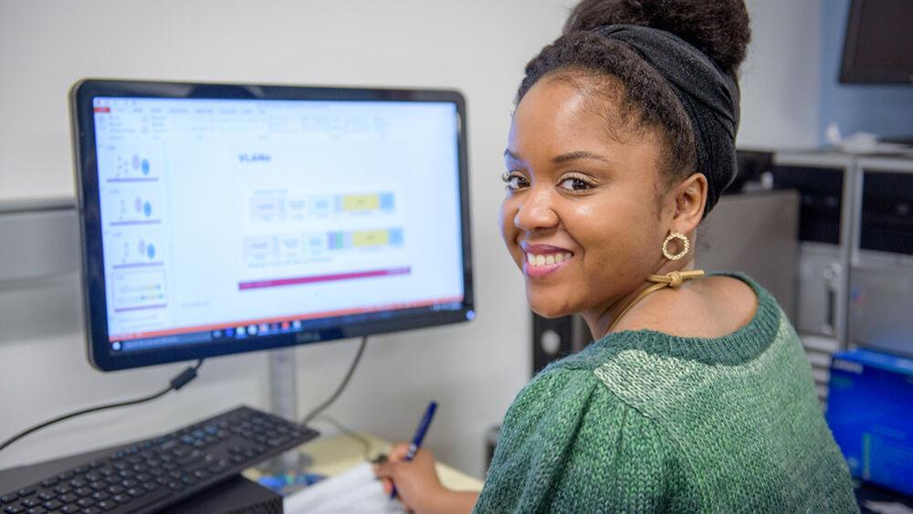 A person smiling to the camera while working on a computer.