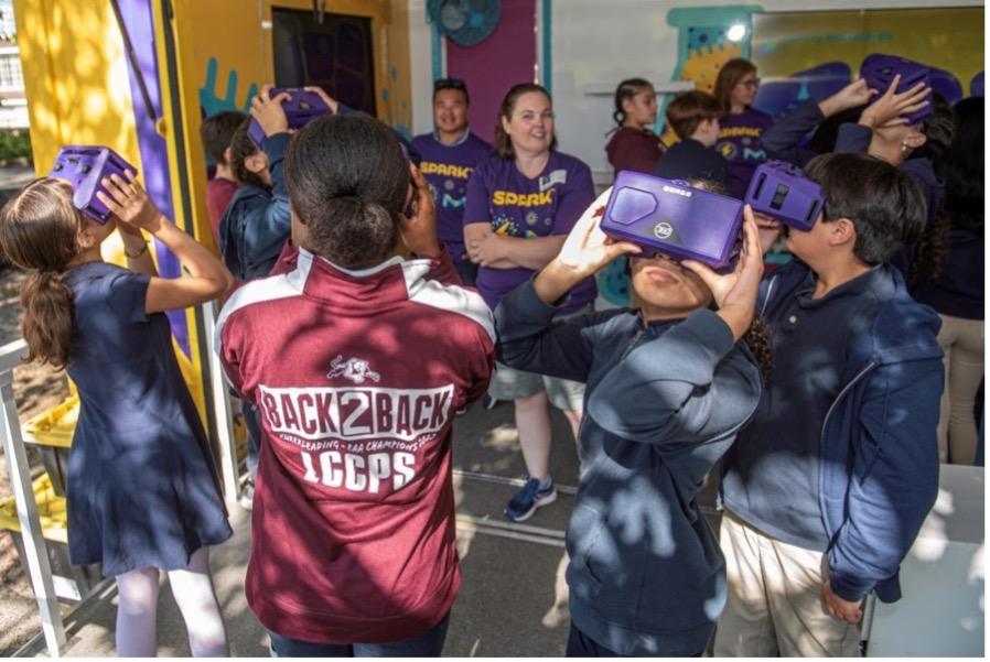 A group of students are interacting with purple VR headsets on the Curiosity Cube.