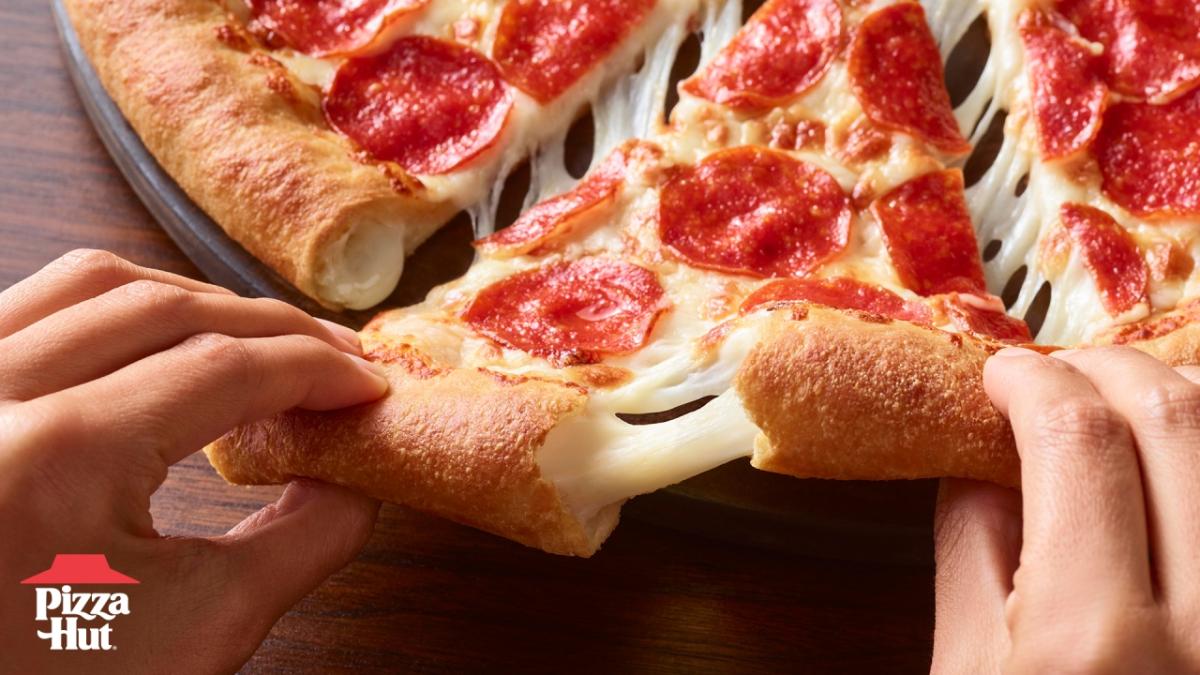 two hands pulling a piece of pepperoni pizza from the pan, cheese stretching from the crust