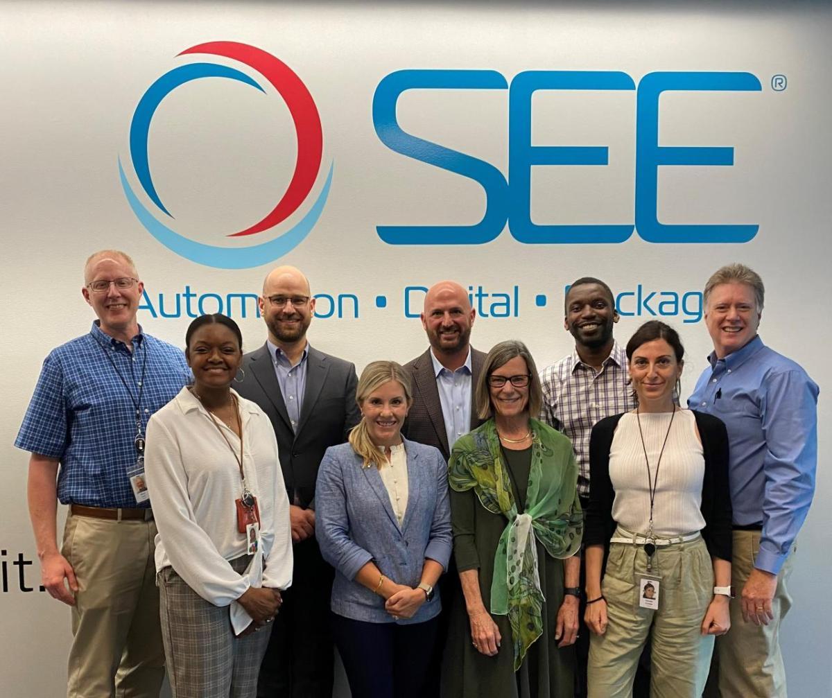 Leaders from the Plastics Industry Association visit SEE’s headquarters to discuss the ways innovation and collaboration enhance the circularity of essential plastic packaging. A group of people stand in front of the SEE company logo facing the camera.