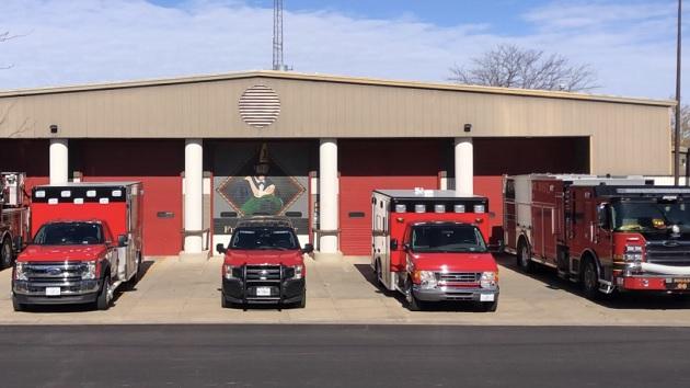 A row of first response and fire vehicles lined up outside a fire station.