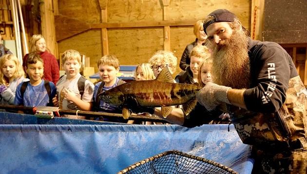 A person holding up a fish to a group of young children