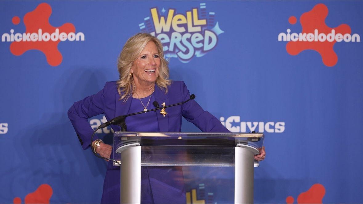 A person stood at a stand at the “Well Versed” premiere, talking into a microphone 