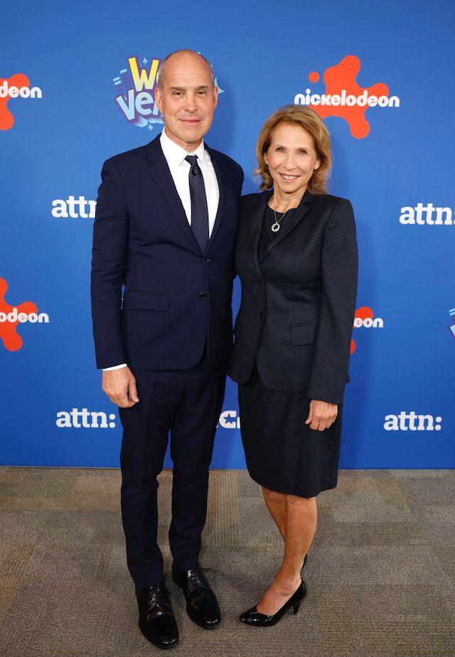 Two people stood together wearing suits in front of a nickelodeon logo backdrop