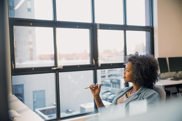 Woman sitting at her desk at work and looking out of a window.