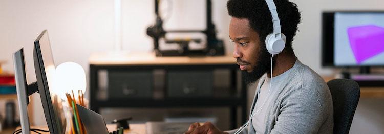 Black male wearing headphones is seated in front of a computer.