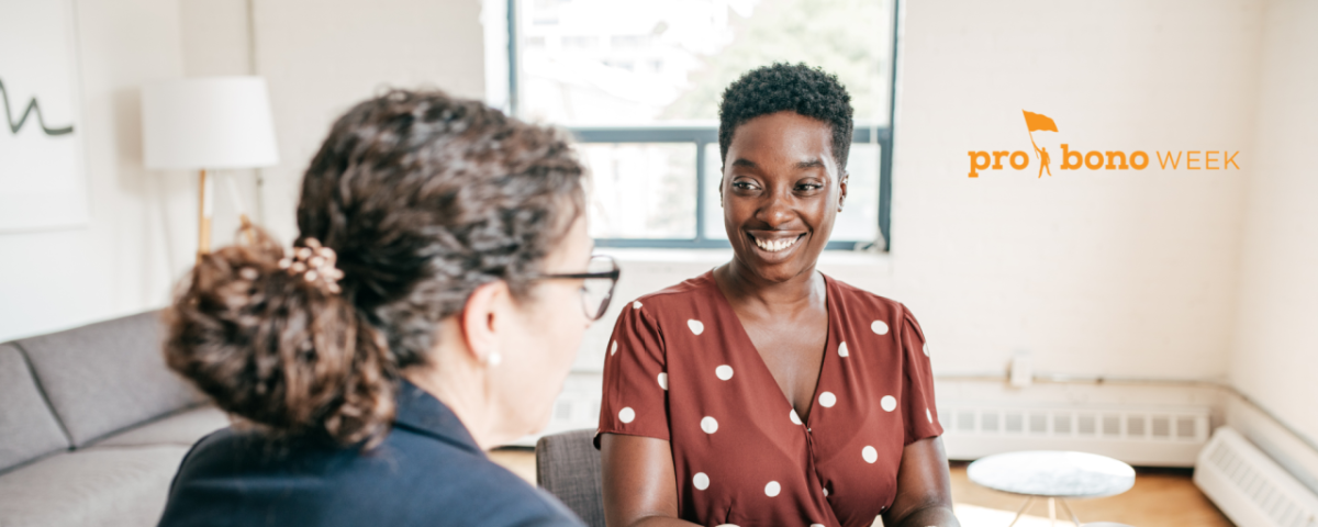 two smiling women talk at a table in a white room