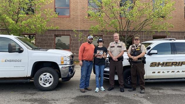 (TOP PHOTO: From left, Enbridge mechanical technician Ryan Humphrey, his son Jackson, Beltrami County Sheriff Jason Riggs and Beltrami County Sgt. Rob Billings.) Two people stood next to two Sheriff’s and their cars