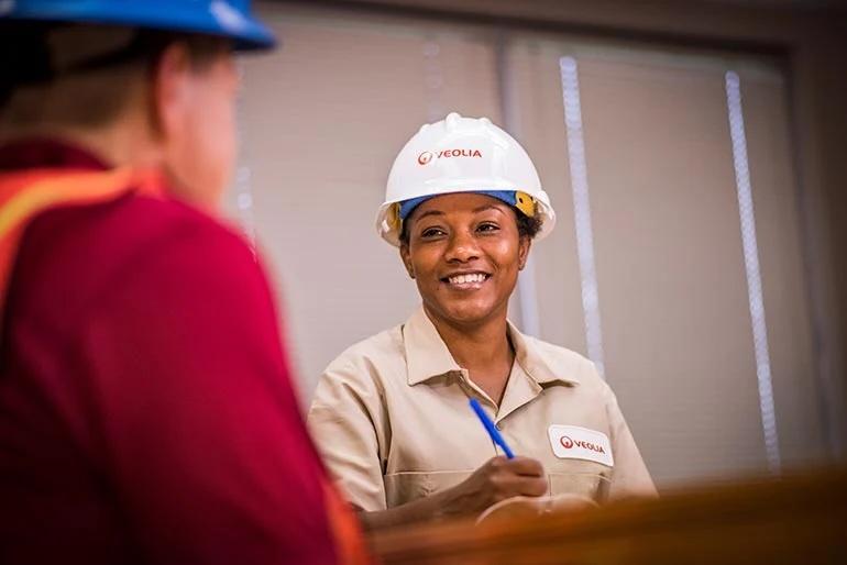 Veolia worker in a hardhat speaking to someone and taking notes