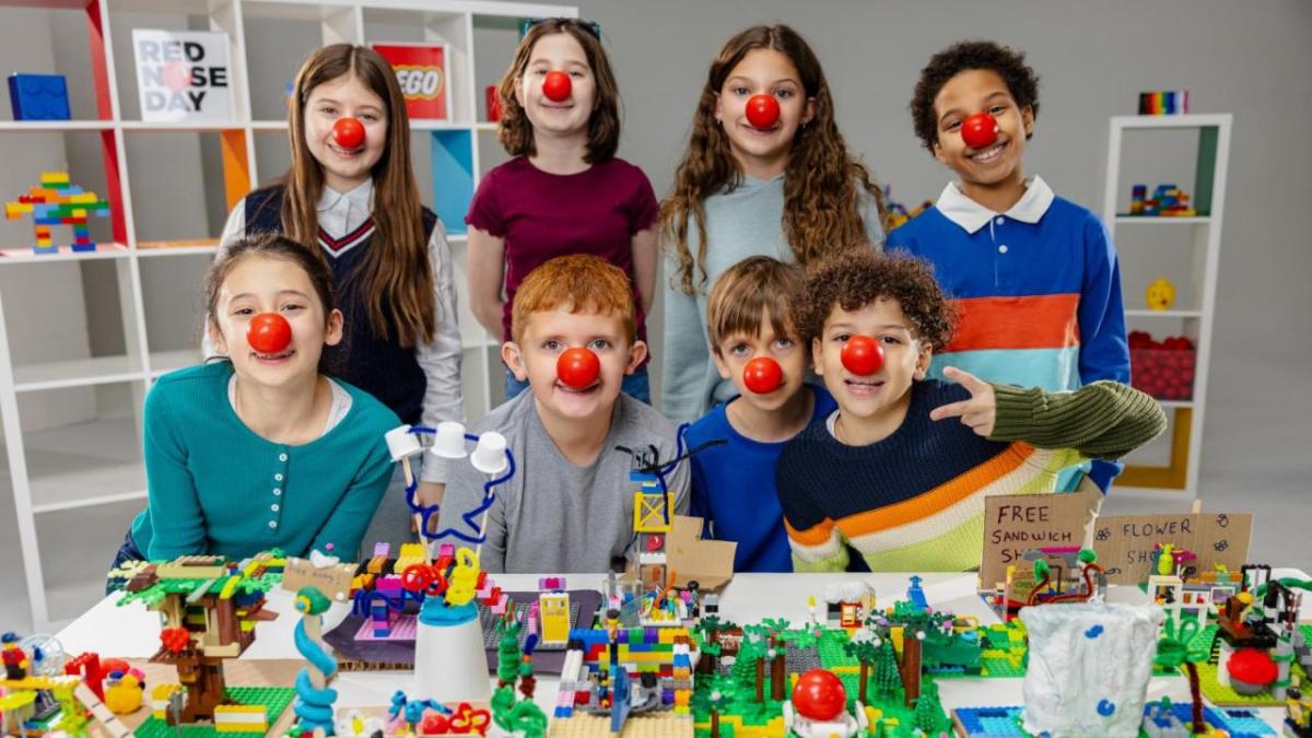 Children wearing red noses behind a table with lego models on 