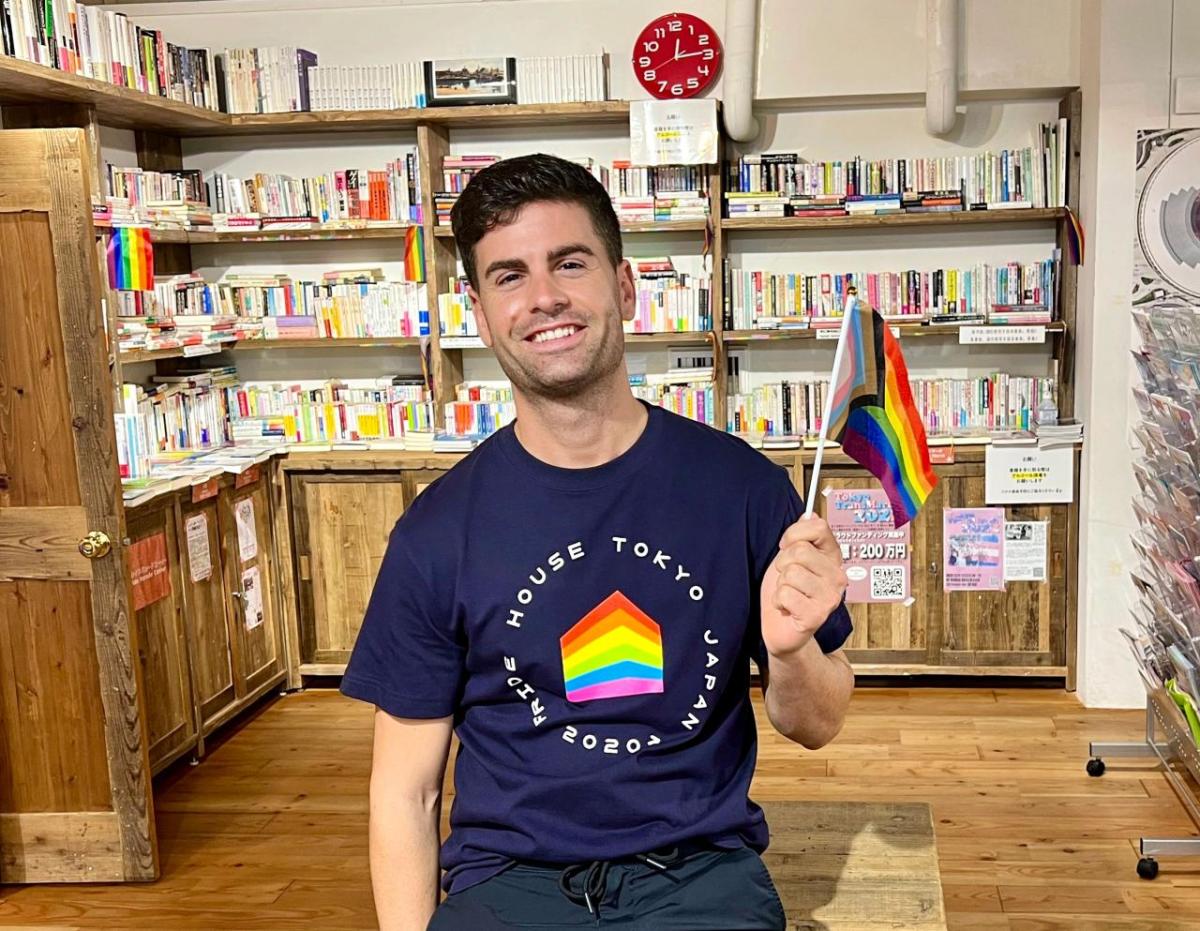 Javier Raya with a small pride flag in a room full of books.