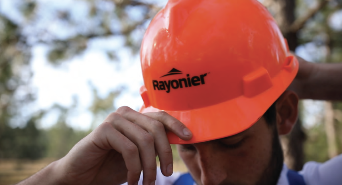 A person putting on a red safety hat with the Rayonier logo on the front