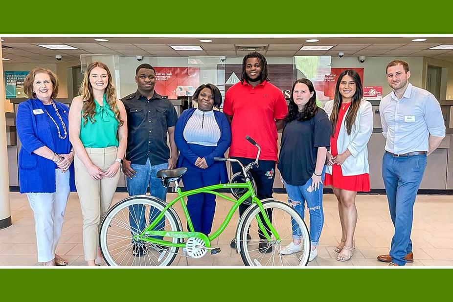 a group of eight people standing in a bank lobby, a green bicycle in front of them