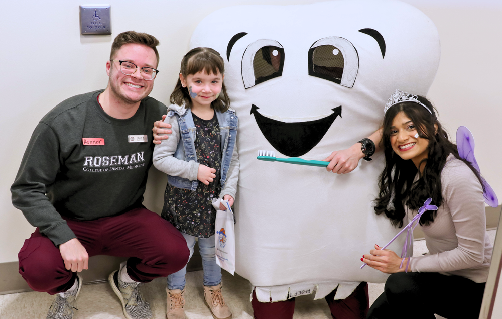 Two adults and a child next to a tooth mascot