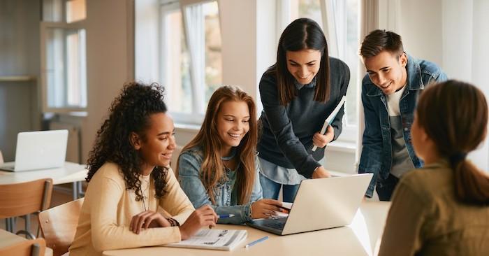 Teacher working with a group of four students who are seated behind a laptop.