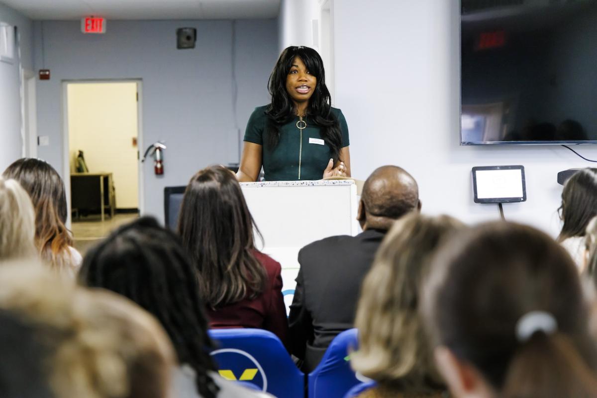 Photo: SCO client, Chrissa B. speaking at the podium and sharing from her journey, “I want my son to grow as much as I am.”