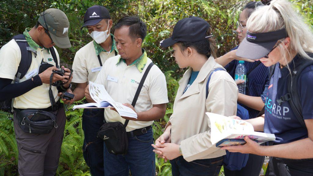 A group of six people outside looking at bird guide books. One carries a camera.