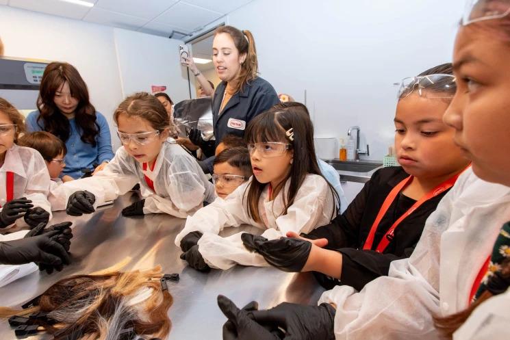 Children and adults in protective lab gear surround a table.