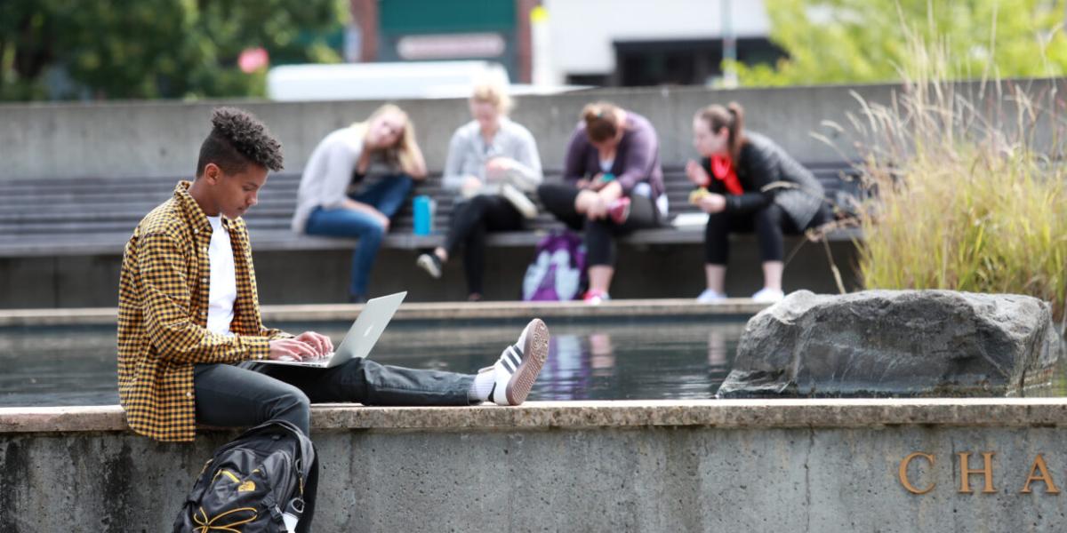 Yosef Chaim Kalinko; Seattle University Student sat on a wall using their laptop