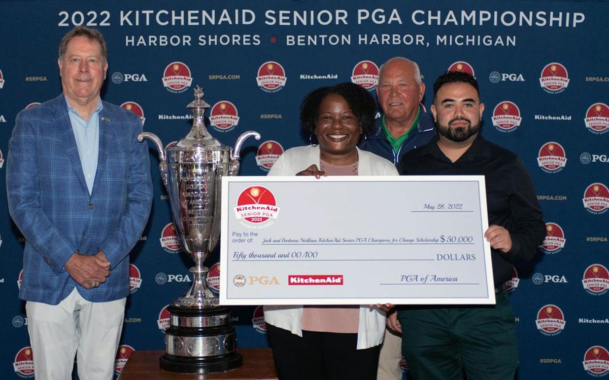Both scholarship winners stand with a large check next to the PGA trophy and two presenters