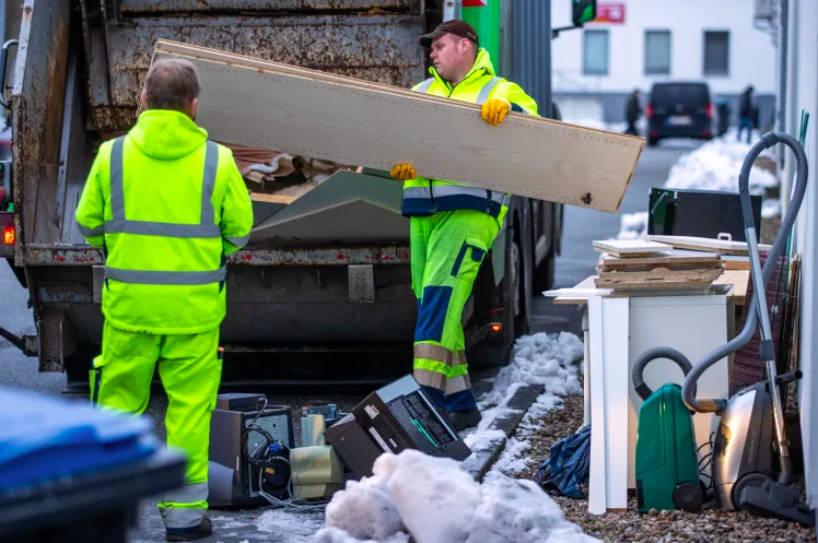 Men throwing old furniture boards into a garbage truck.