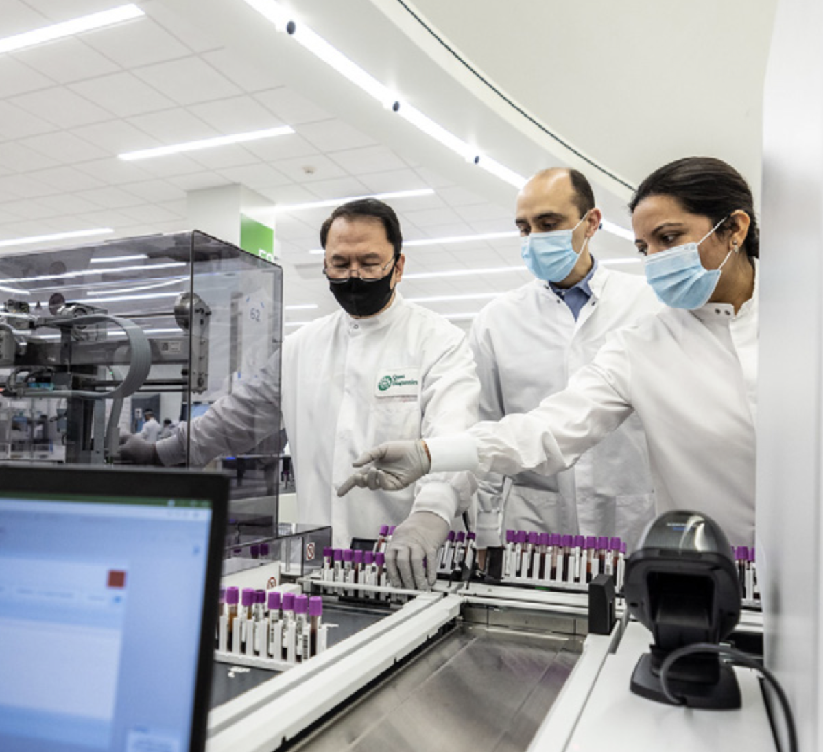 workers in white lab coats and face masks looking over test tubes