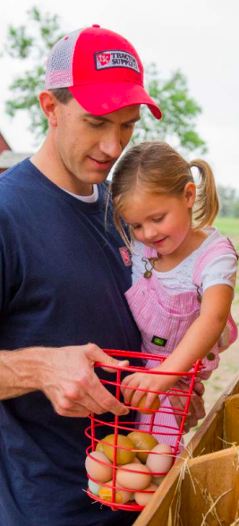 a man carrying a little girl who is putting eggs in a basket