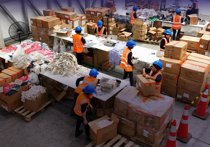 Women wearing safety helmets and high-visibility vests sort and pack materials inside a warehouse at ZEDE Posorja in Ecuador.