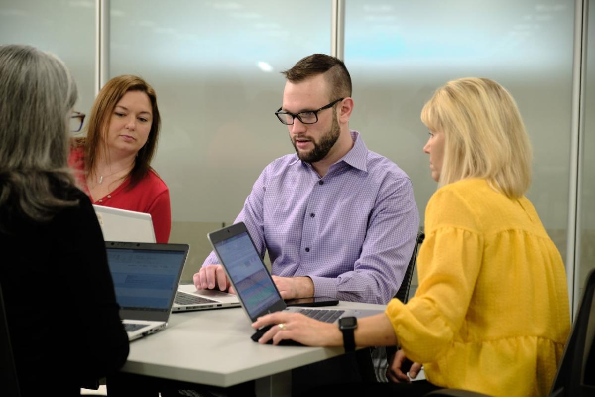 Richard McMichael works on his laptop while two coworkers look on