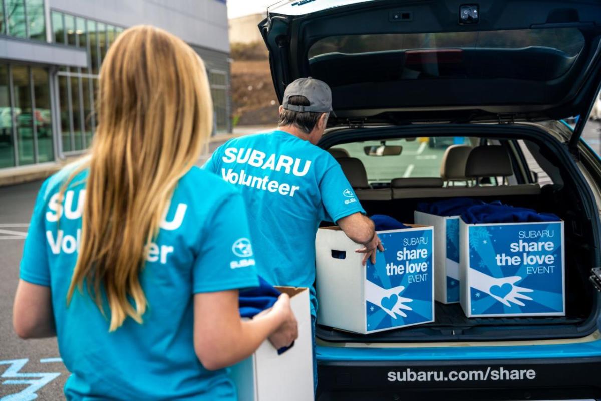 two Subaru volunteers loading donation boxes into the boot of a car