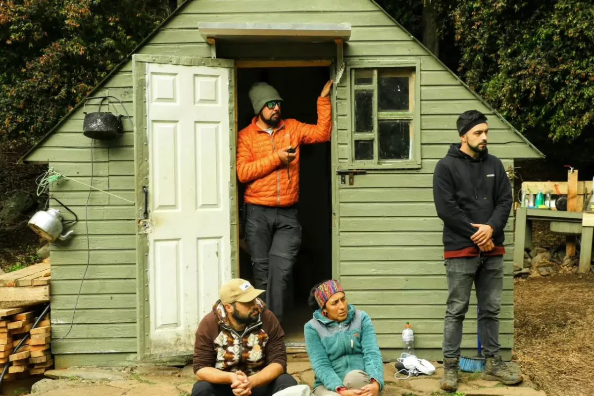 A green shed with a person stood in the doorway and another to the right, with two people sat on the floor