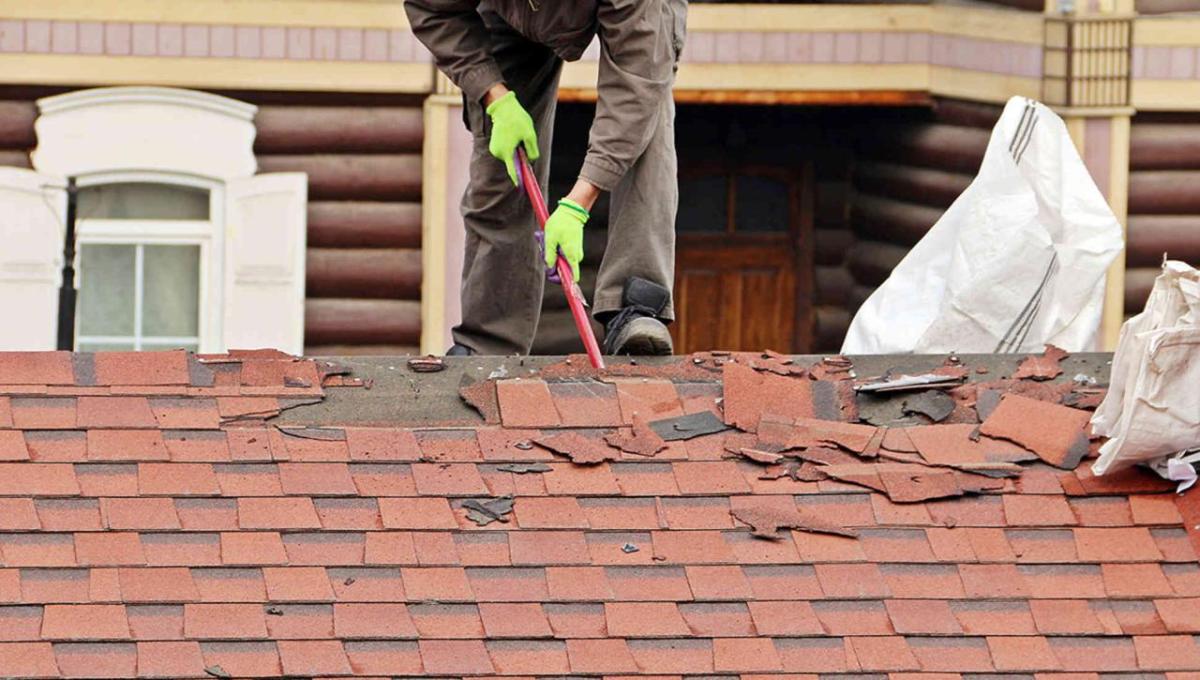 A person taking shingles off of a roof
