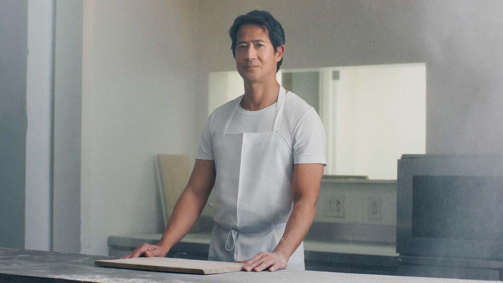 A baker wearing an apron stood behind a counter