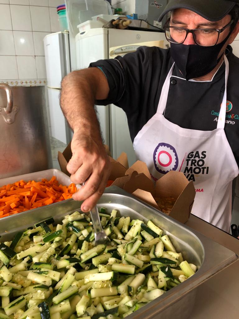 Inside a kitchen, a man stirs fresh food in a large metal vessel.