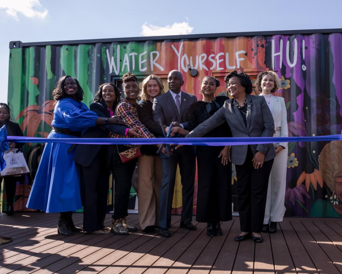 8 people cutting ribbon of a SheCare pod at Hampton University