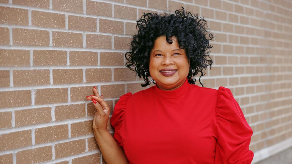 Stacey Bledsoe in a red shirt leaning against a brick wall.