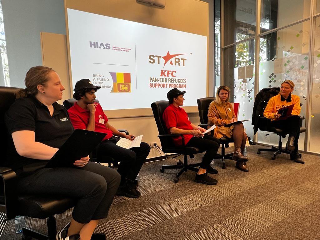 People seated in a room, some in KFC uniforms. "Start KFC" projected on a screen behind them. 