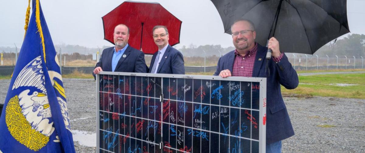 Three men holding umbrellas at opening of facility