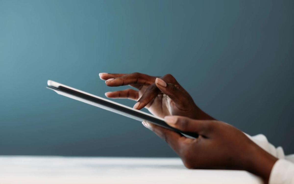 Close-up of a person’s hands using a digital tablet, with fingers gently tapping the screen against a soft blue background.